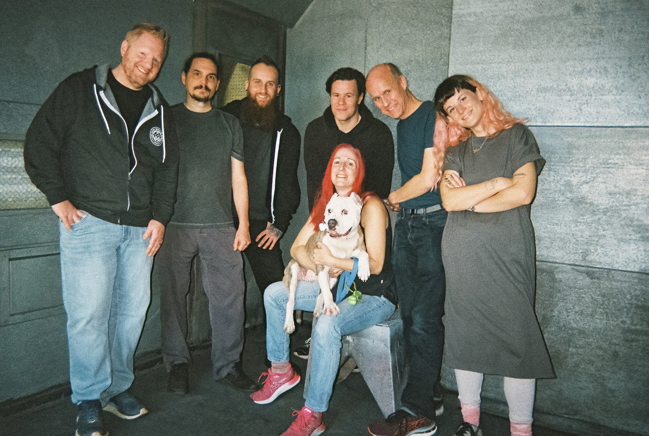 The Noise Engineering team standing against an industrial background with Kris holding Alice the dog